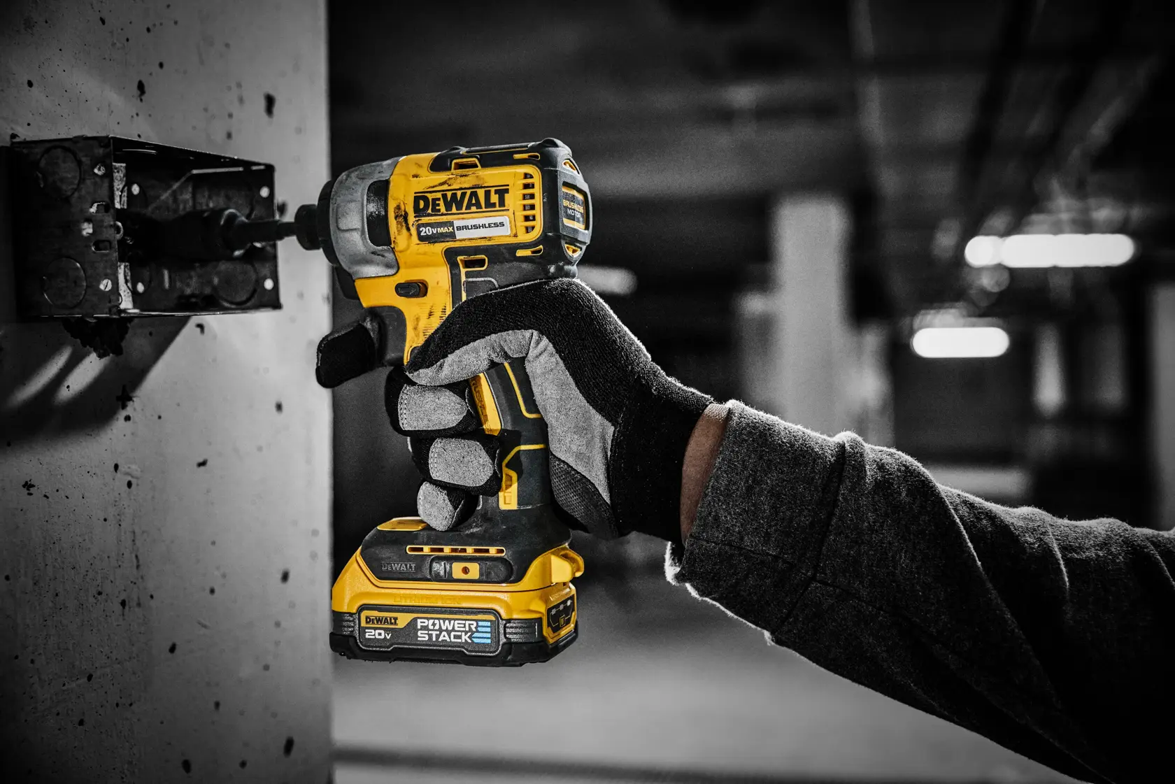 Um trabalhador com luvas e botas de trabalho usa uma ferramenta elétrica sem fio amarela e preta da DEWALT com uma bateria DCBP034 em um canteiro de obras. A ferramenta está sendo usada para perfurar concreto ou pedra e está conectada a um acessório de extração de poeira.
