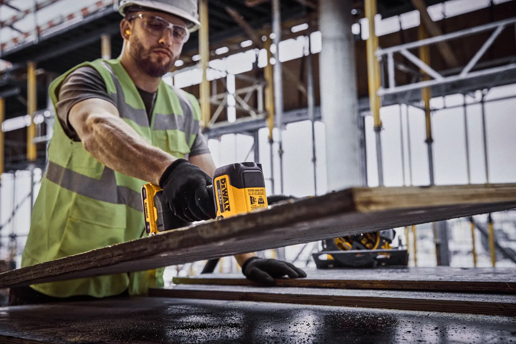 Uma pessoa vestindo colete de segurança e luvas está usando uma ferramenta DEWALT para medir ou inspecionar uma tábua de madeira em um canteiro de obras.