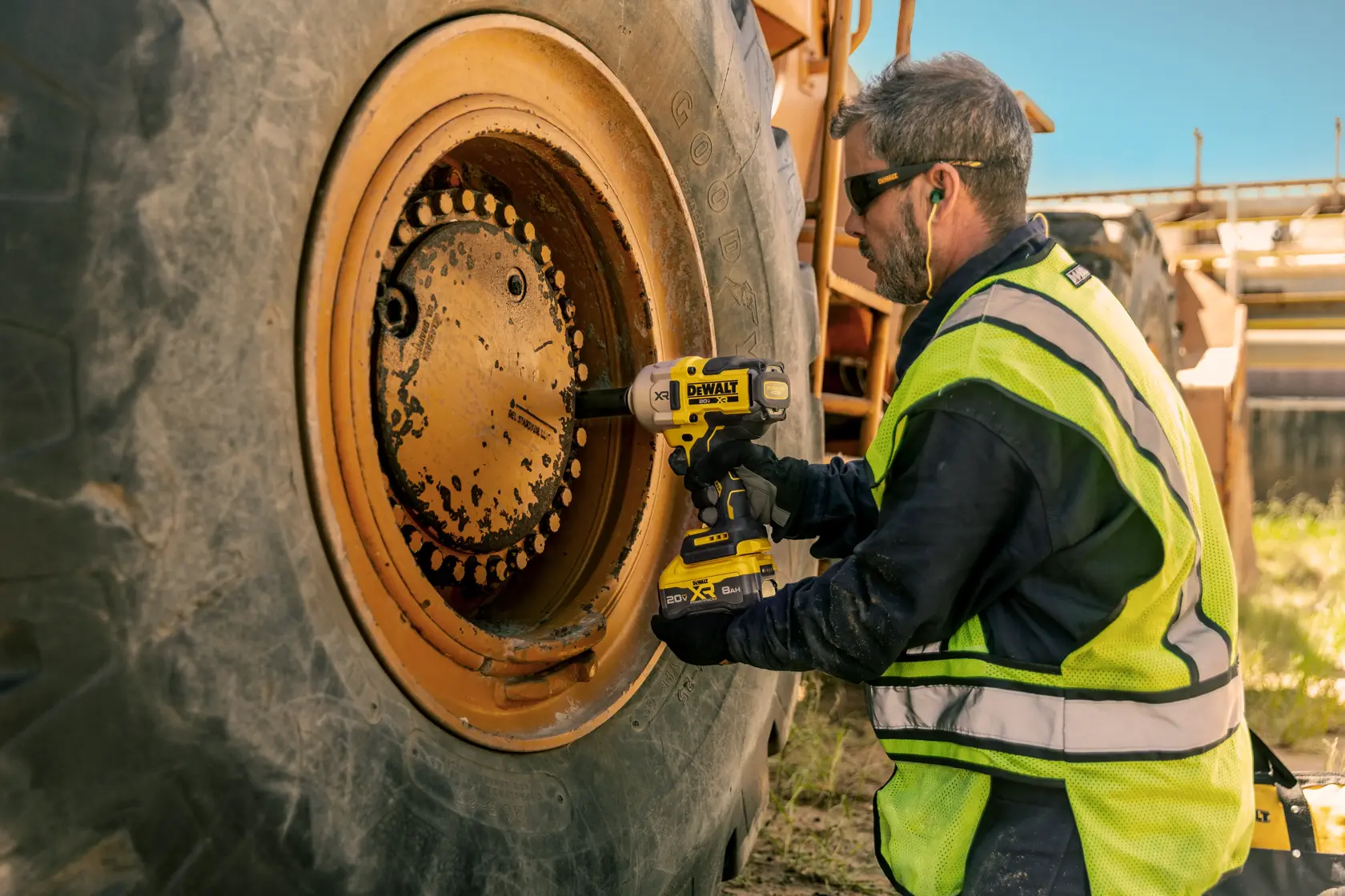 Pessoa utiliza chave de impacto DEWALT para apertar parafusos em roda de veículo industrial grande ao ar livre.