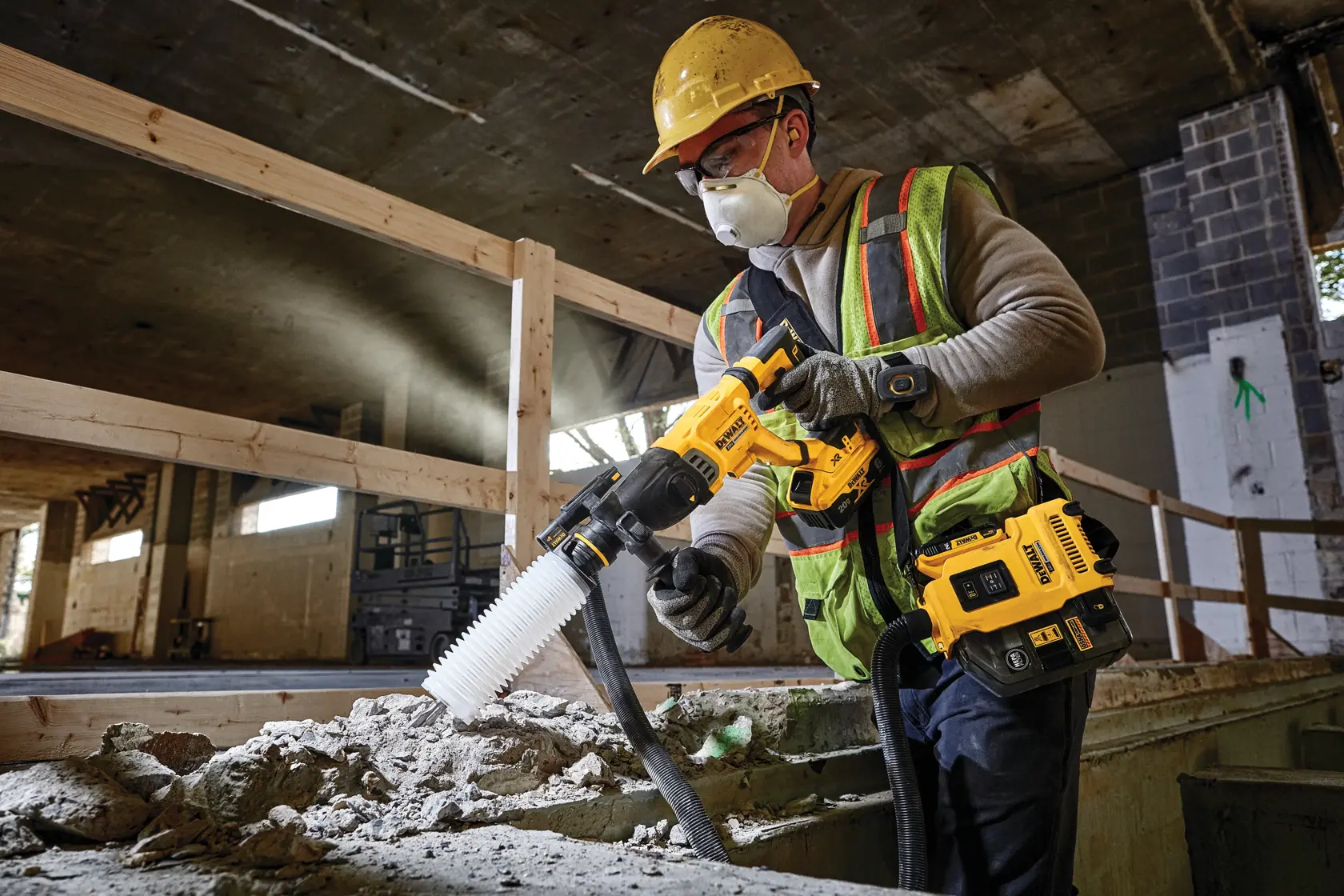Um trabalhador da construção civil usando capacete amarelo e colete de segurança opera uma ferramenta elétrica DEWALT com acessório de aspirador, perfurando concreto em um canteiro de obras.