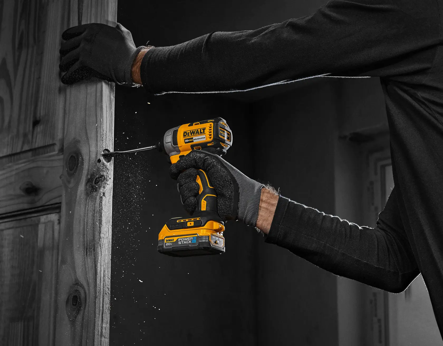 Una persona con guantes negros está usando un taladro inalámbrico DEWALT para perforar una superficie de madera, con aserrín visible alrededor de la broca.