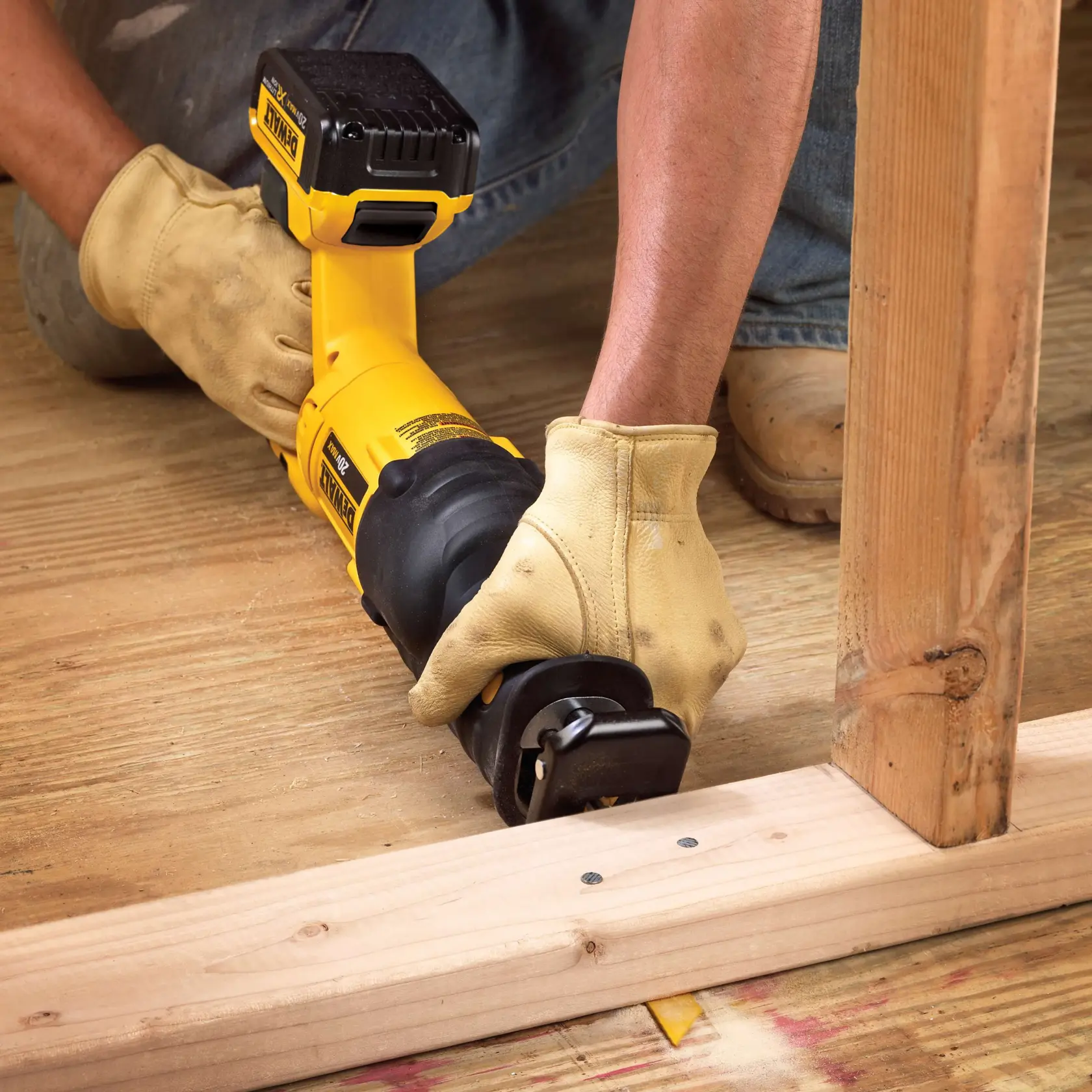 Uma pessoa usando luvas de trabalho amarelas está utilizando uma serra recíproca sem fio DEWALT amarela para cortar madeira em um canteiro de obras. A serra está posicionada próxima a uma viga de suporte de madeira e um piso de tábuas de madeira.