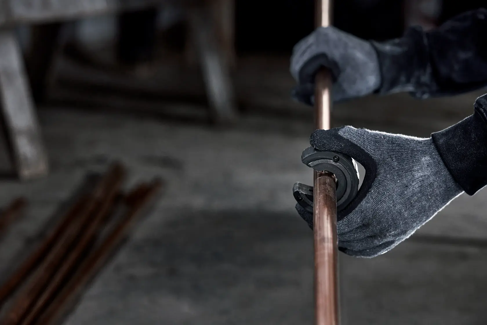 Una persona con guantes utiliza una herramienta eléctrica DEWALT para cortar un tubo de cobre. Varios tubos de cobre están en el suelo cerca.