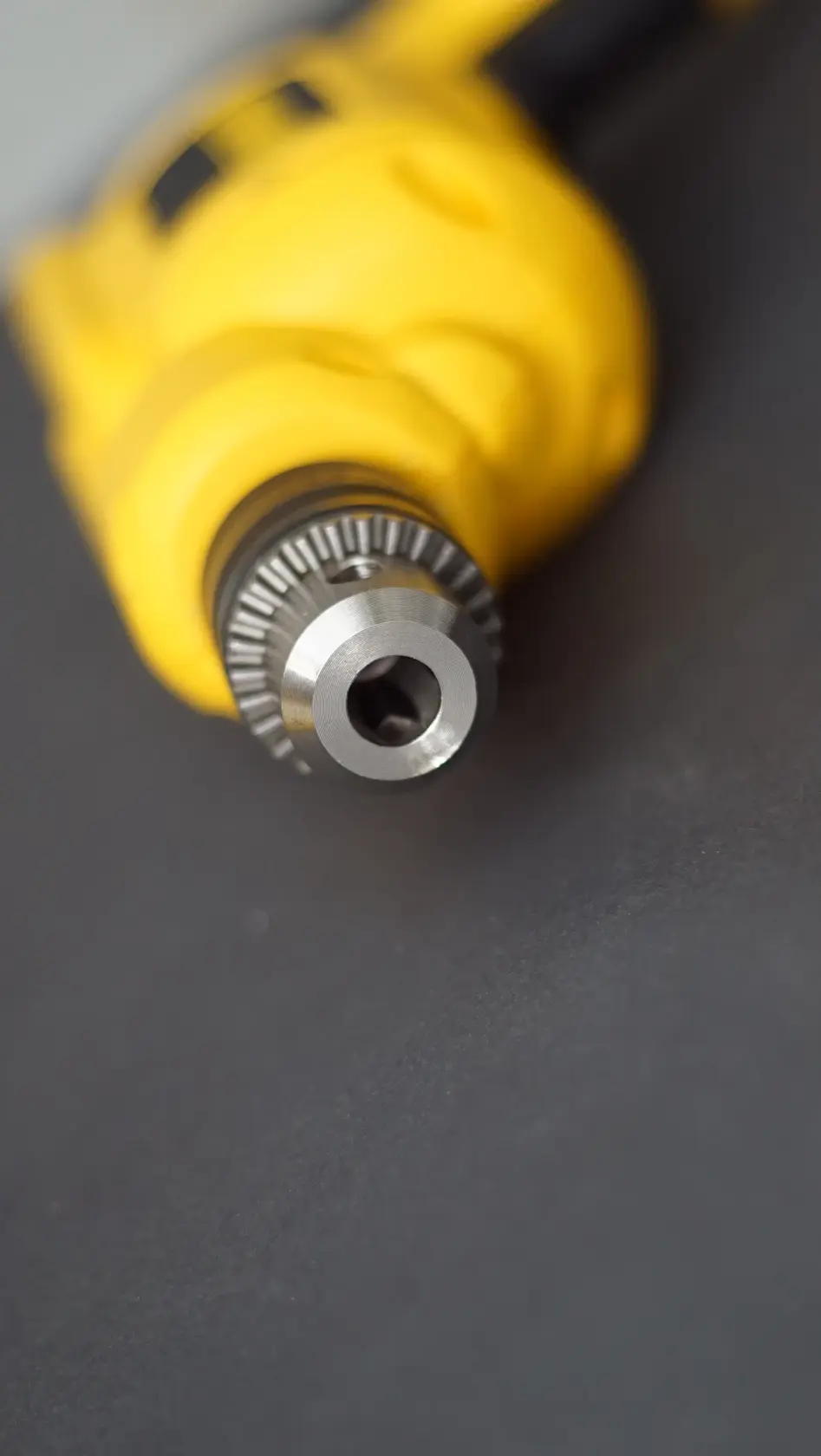 Primer plano del portabrocas metálico de un taladro eléctrico amarillo, enfocado en la cabeza del taladro sobre una superficie oscura.