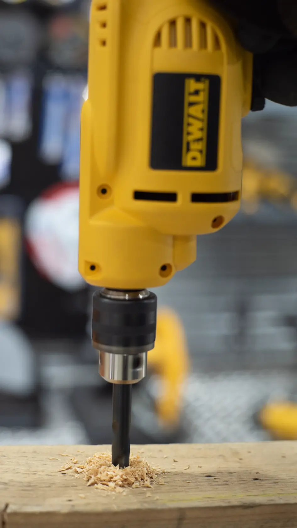 Vista de cerca de un taladro eléctrico amarillo DEWALT perforando una tabla de madera, con virutas de madera acumulándose alrededor de la broca.