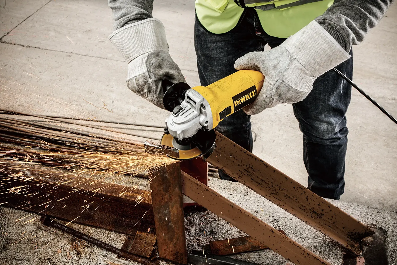 Una persona con guantes de seguridad utiliza una amoladora angular DEWALT DWE4010 para cortar una viga metálica, mientras saltan chispas de la zona de corte.