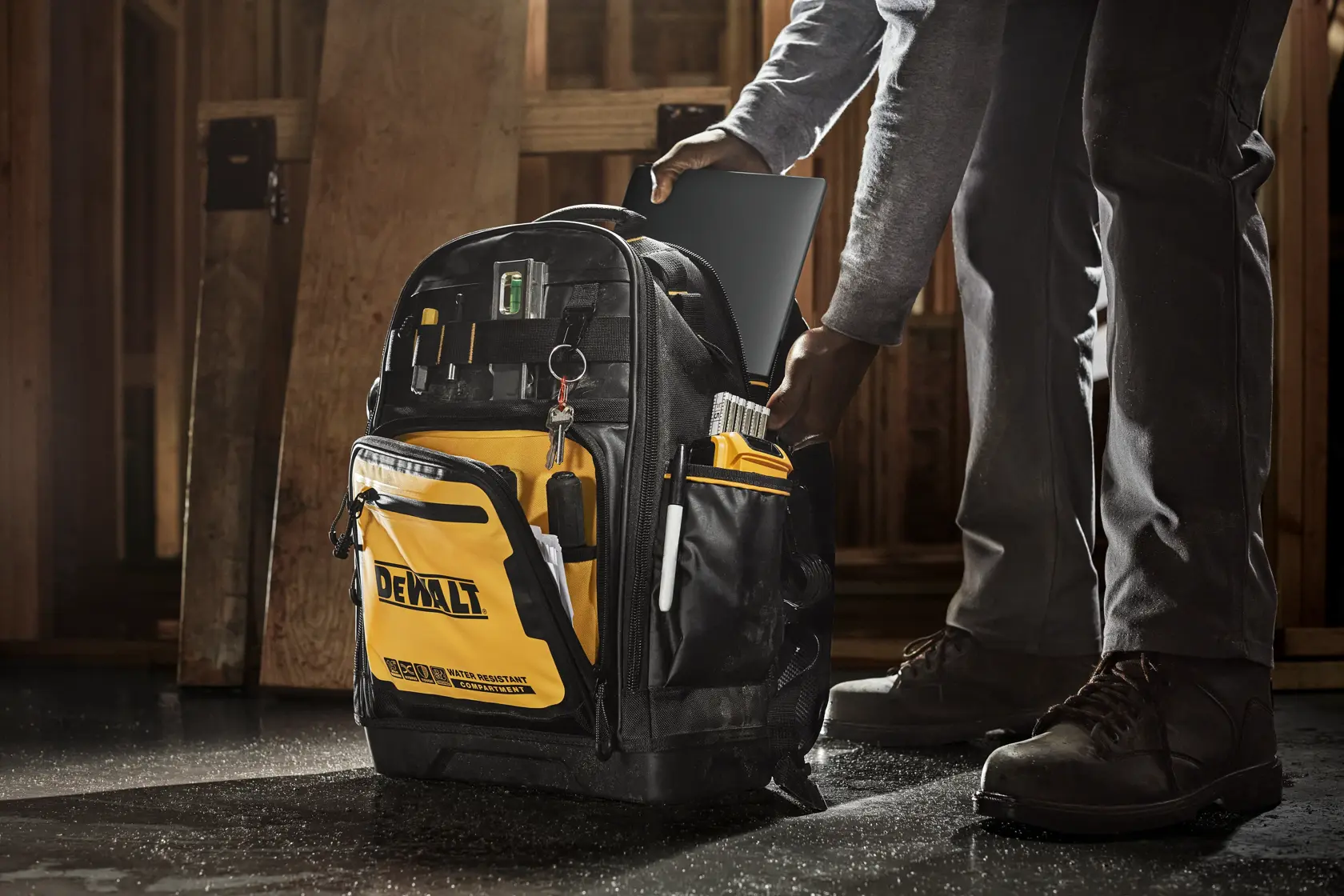 Mochila DEWALT negra y amarilla con varios compartimentos, bolsillos laterales y un compartimento frontal resistente al agua. En la parte delantera se muestra el logo de DEWALT y los iconos para híbrido, táctil y dispositivo de 14 pulgadas, destacando durabilidad y funcionalidad.